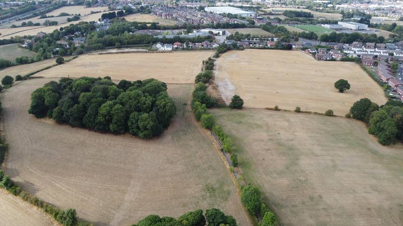 Aerial view from the south showing both fields after harvest, the copse between them, and Barnsley in the distance.