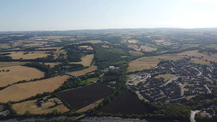 High oblique aerial view south-west across open countryside and a wooded ridge towards the motorway.